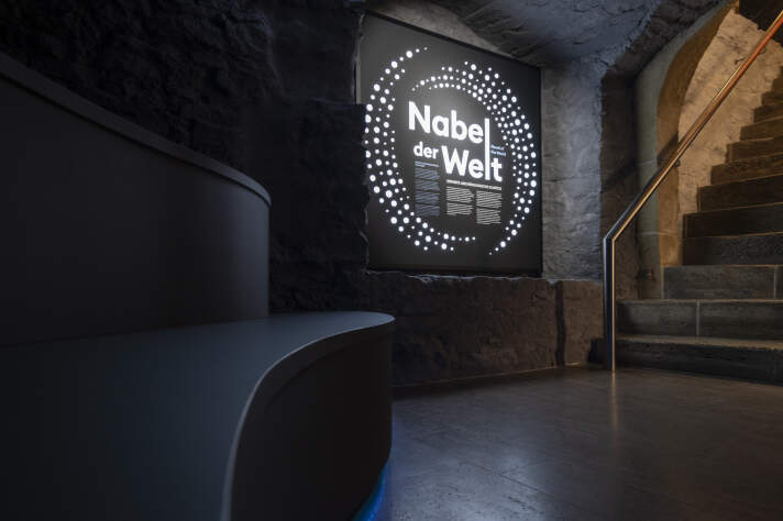 Dauerausstellung „Nabel der Welt“ – Eingangsbereich Grafik mit Leuchtschrift an einer Wand, Schriftzug "Nabel der Welt"